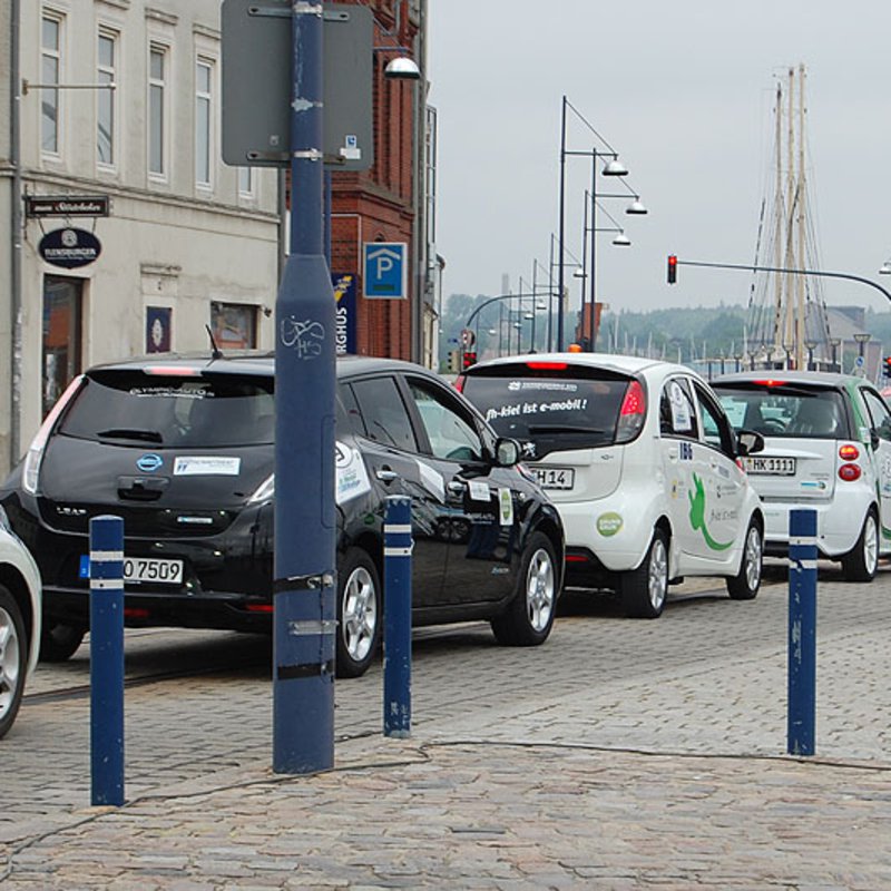 Mehrere kleine E-Autos reihen sich auf einer öffentlichen Straße aneinander.