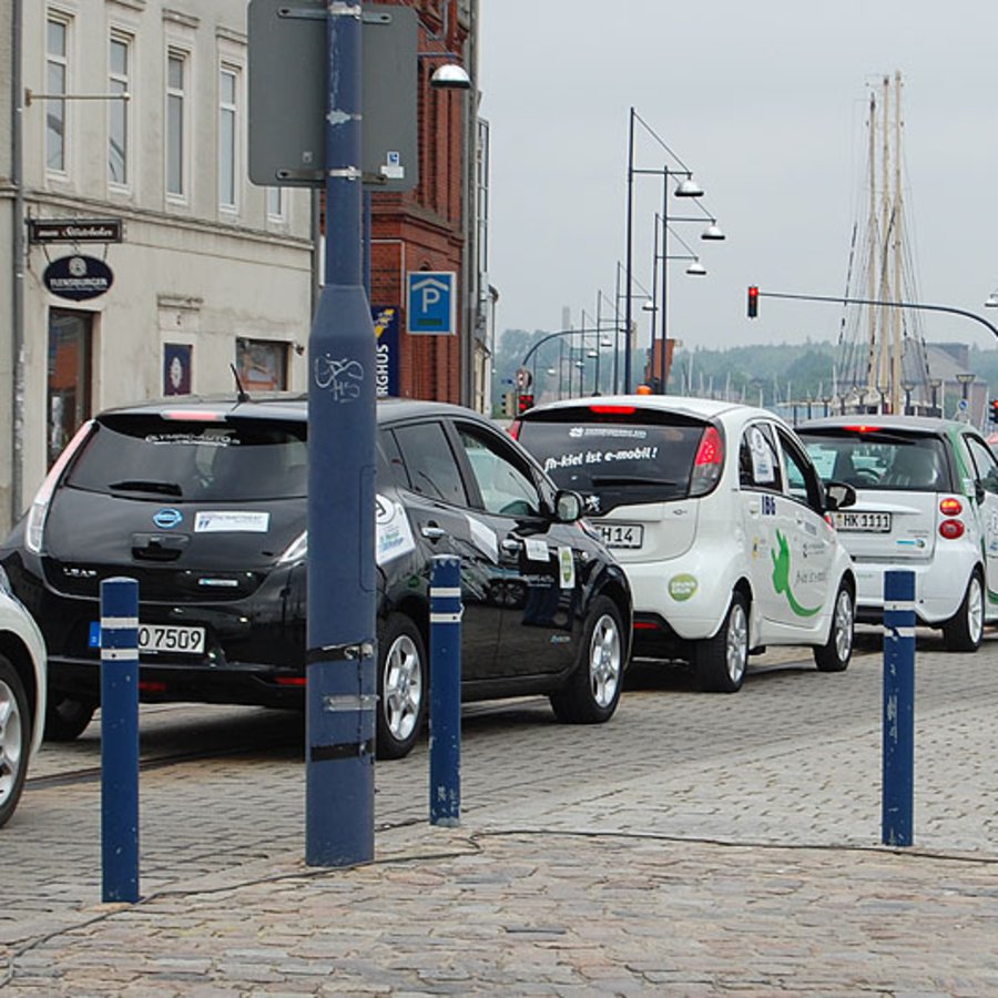 Mehrere kleine E-Autos reihen sich auf einer öffentlichen Straße aneinander.