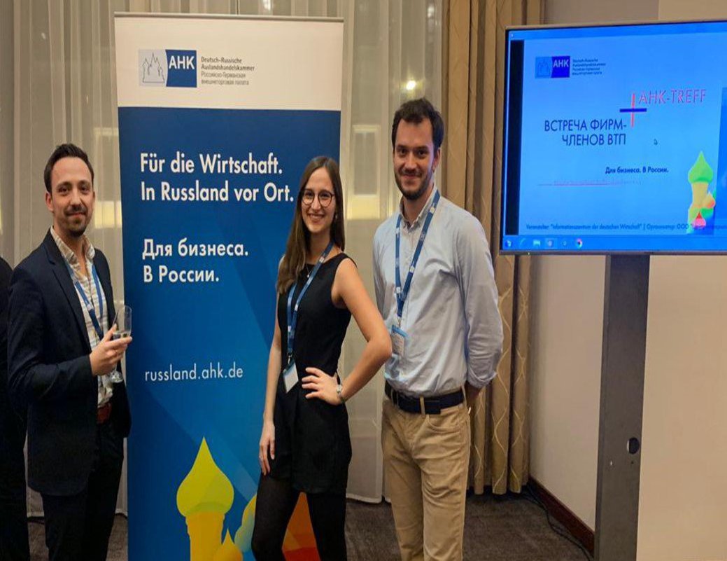 Zwei Männer und eine Frau posieren vor einem Infostand.