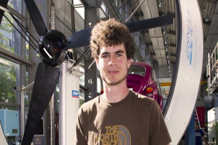 Ein Student steht vor dem mächtigen Propeller, eines Gegenwindrennwagens.