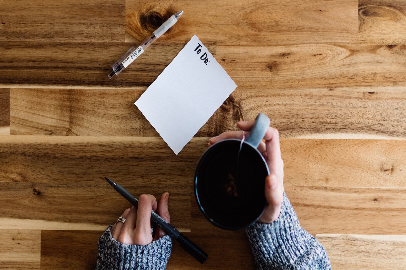 zwei Hände mit Becher, Zettel und Stift auf einem Tisch