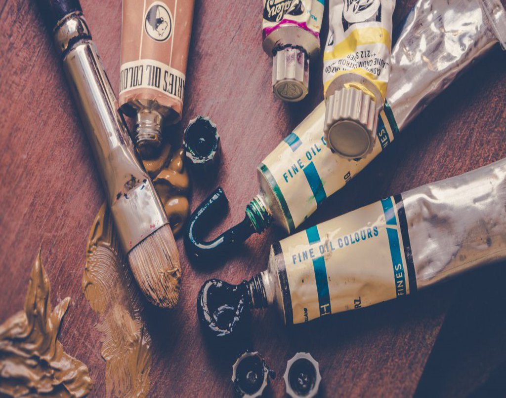 Geöffnete Farbtuben aus denen Farbe austritt, nebendran liegt ein dicker Holzpinsel.