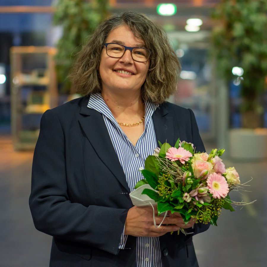 Ein Foto für Ihre Berichterstattung können Sie hier herunterladen. Professorin Dr. Ruth Boerckel, die Dekanin des Fachbereichs Wirtschaft und künftige Vizepräsidentin der FH Kiel steht im Foyer des Mehrzwecksgebäudes und hält einen Blumenstrauß in Händen.