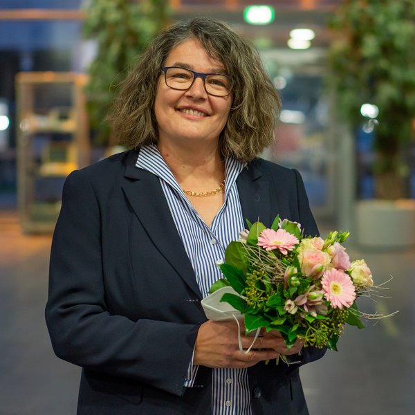 Ein Foto für Ihre Berichterstattung können Sie hier herunterladen. Professorin Dr. Ruth Boerckel, die Dekanin des Fachbereichs Wirtschaft und künftige Vizepräsidentin der FH Kiel steht im Foyer des Mehrzwecksgebäudes und hält einen Blumenstrauß in Händen.