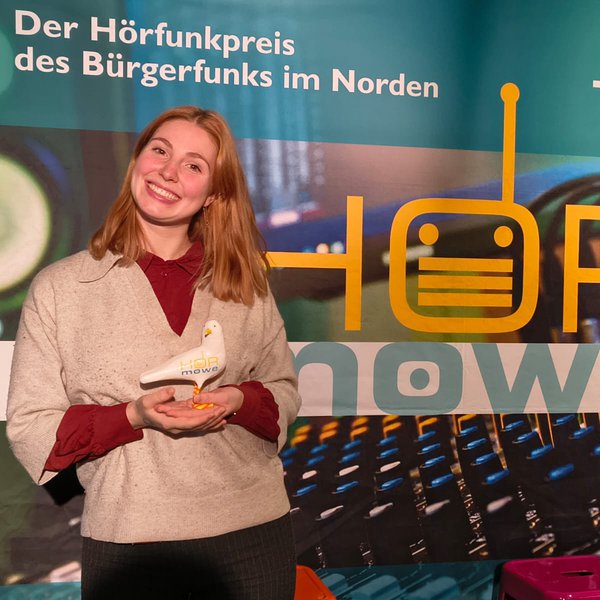 Eine junge Frau, Anja Dencker, hält eine Möwenplastik in der Hand, den Radiopreis HörMöwe wurde für ihre Moderation zum Thema Herzinfarktsymptome bei Frauen mit der HörMöwe ausgezeichnet.