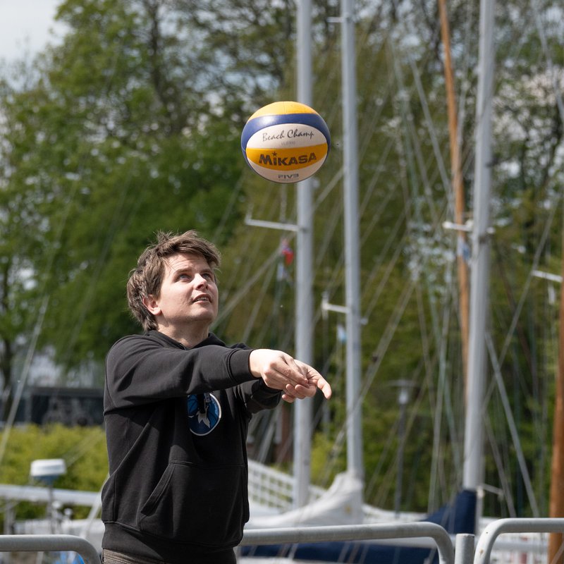 ein Mann spielt mit einem Beach-Volleyball am Steg hinter der Schwentine Mensa in Kiel 