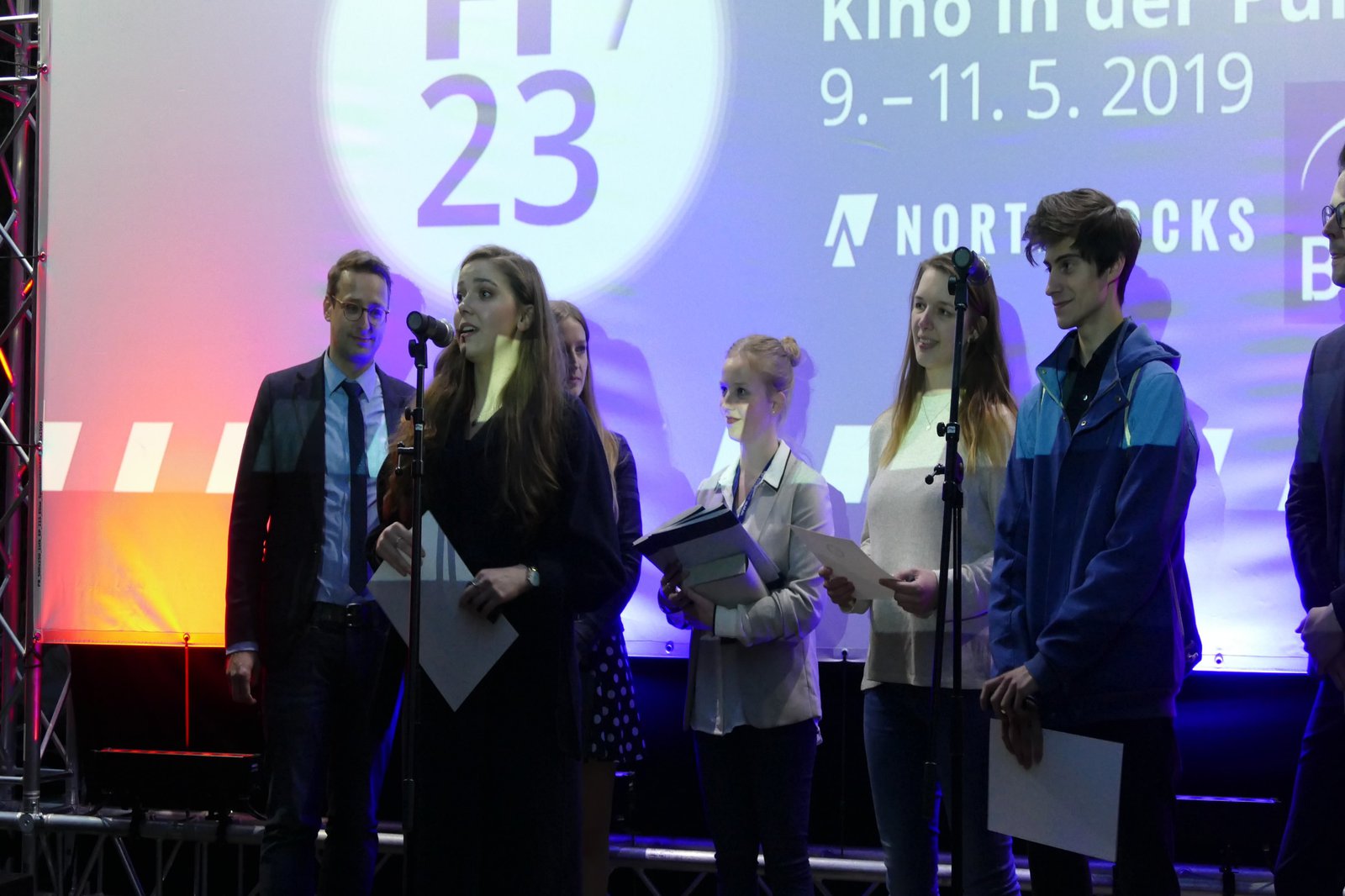 Eine Gruppe an Menschen steht auf einer Bühne und richtet sich an das Publikum.
