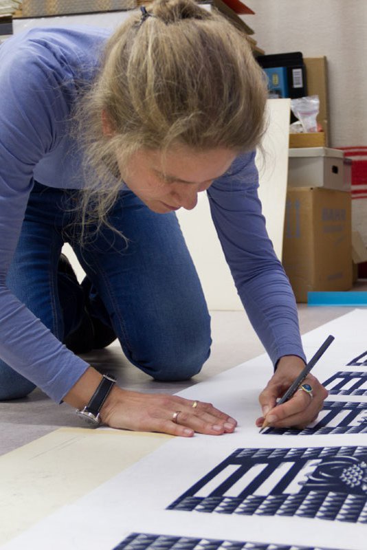 Eine Frau kniet auf dem Boden und manipuliert einen Farbdruck mit einem Bleistift.