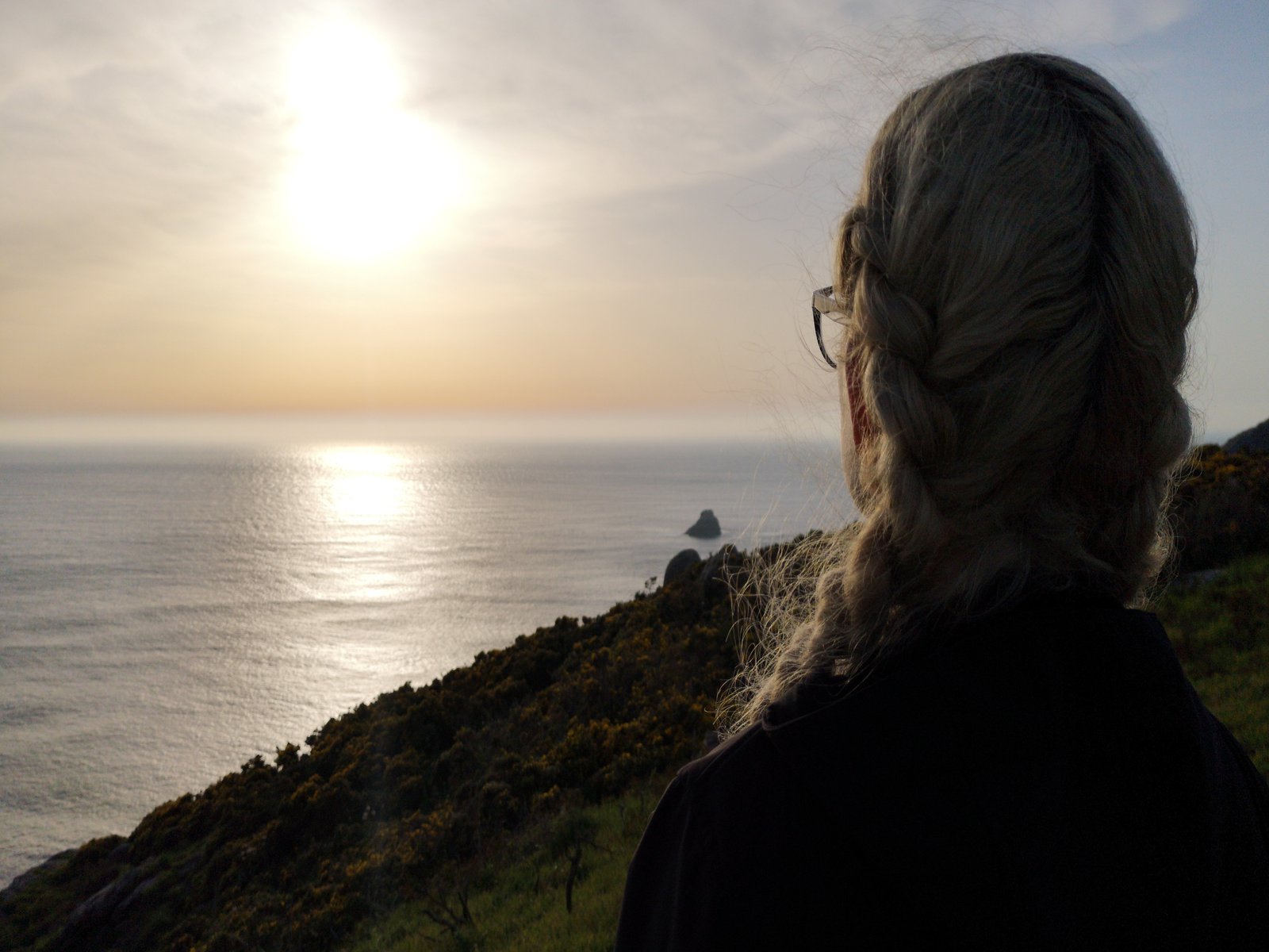 Eine Frau steht an einem Abhang und betrachtet die über dem Meer aufgehende Sonne.