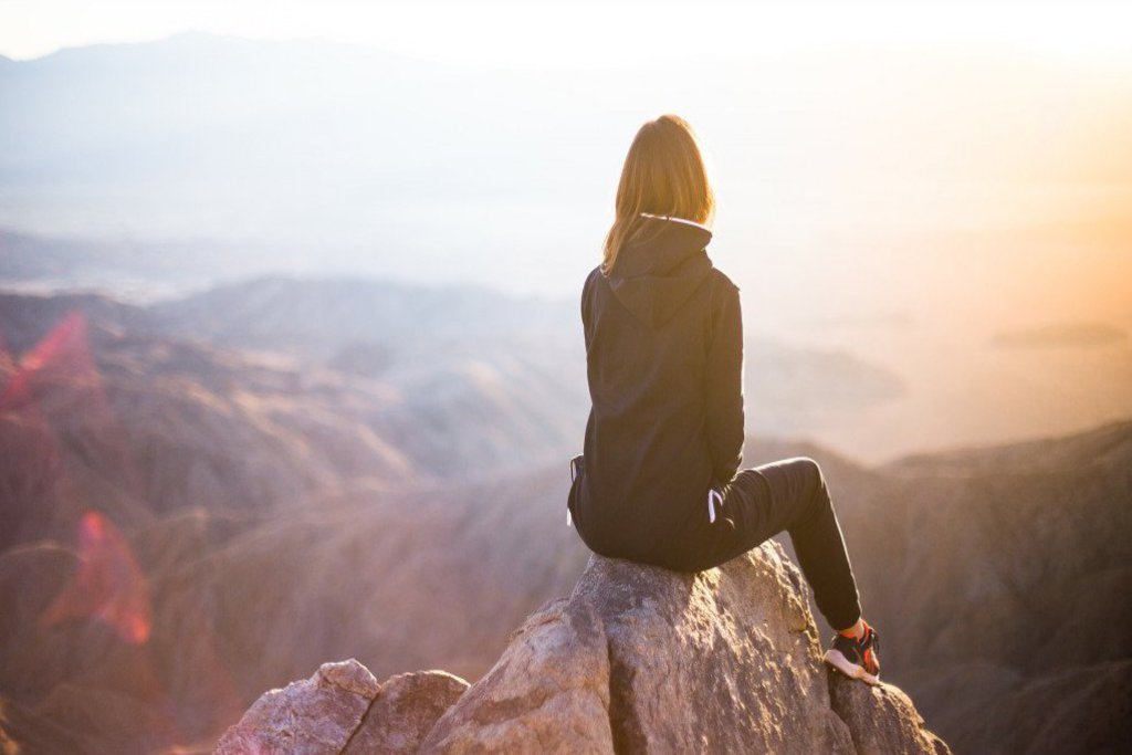 Eine Frau sitzt auf einem Felsen, hoch oben auf einem Berg.