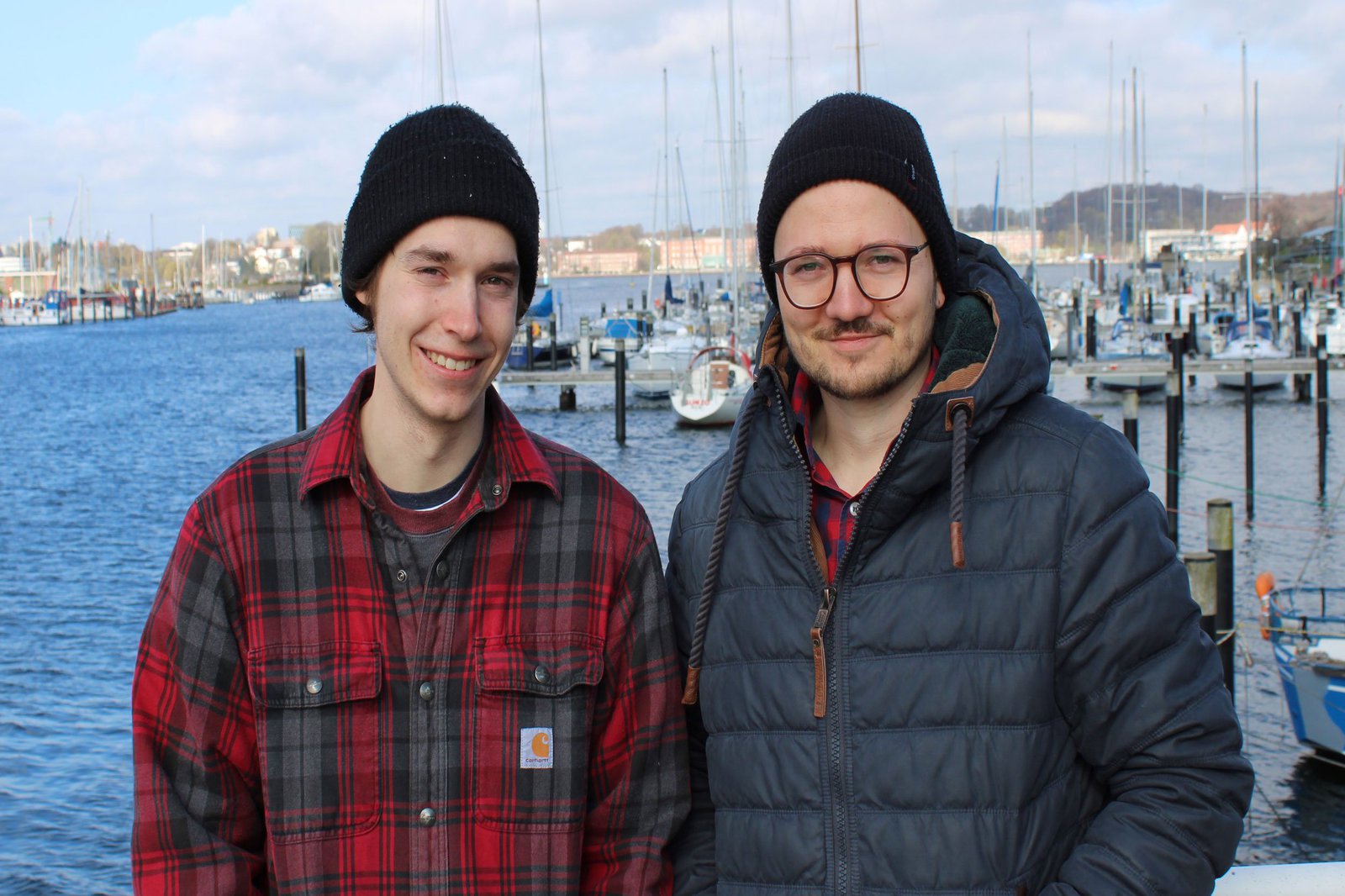 Zwei Männer mit Mütze posieren am Hafen der Schwentinemündung.