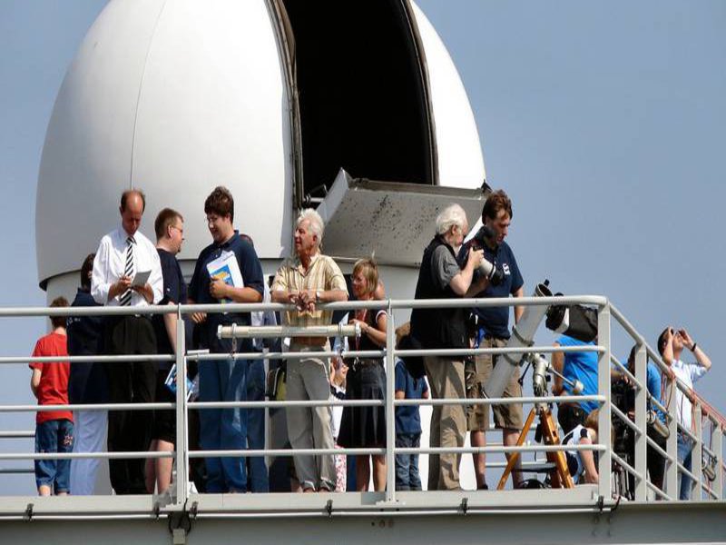 Menschen stehen bei bestem Wetter hoch oben bei der Kuppel einer Sternenwarte.