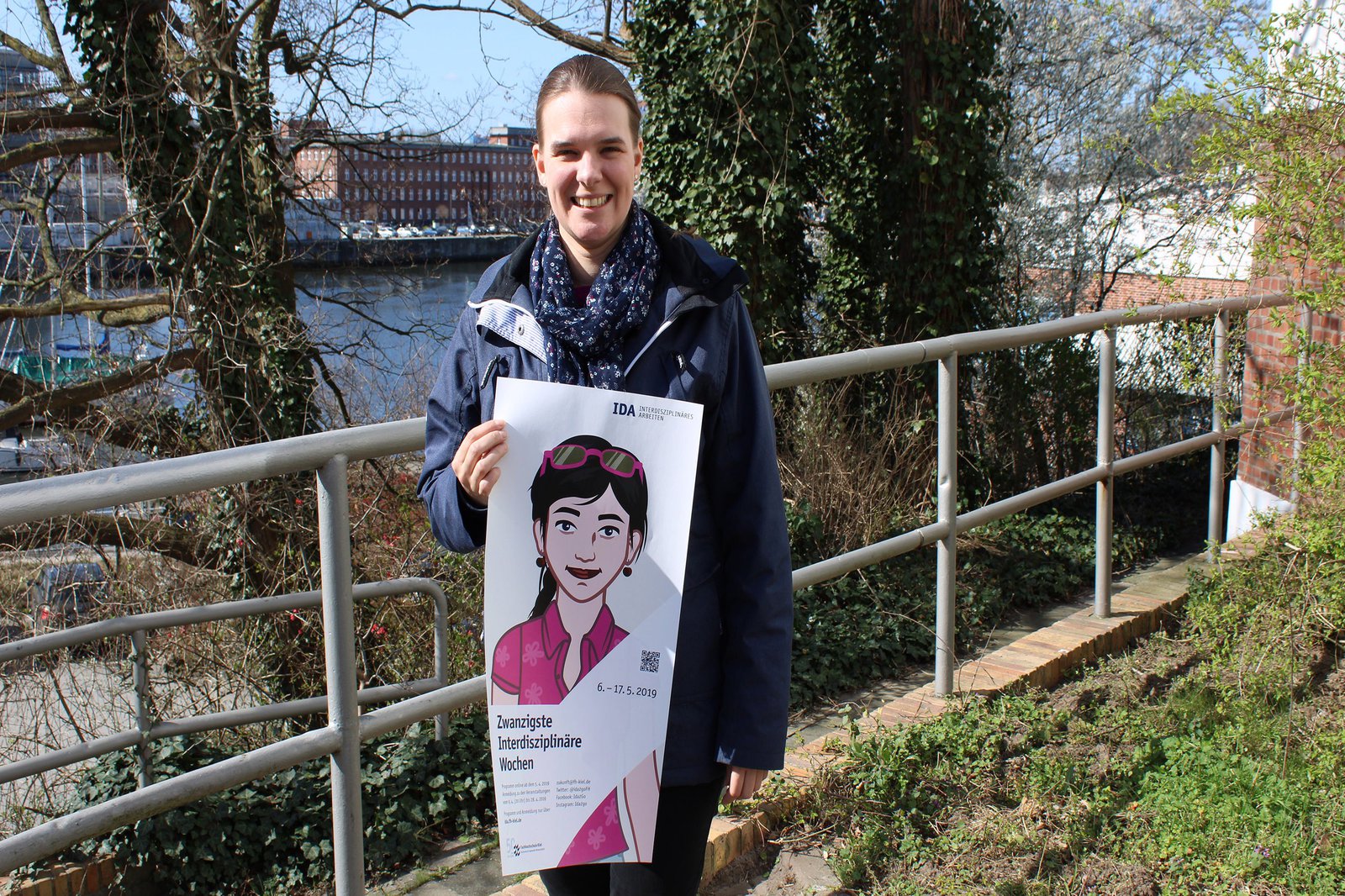 Eine Frau hält lächelnd ein Plakat in die Kamera.