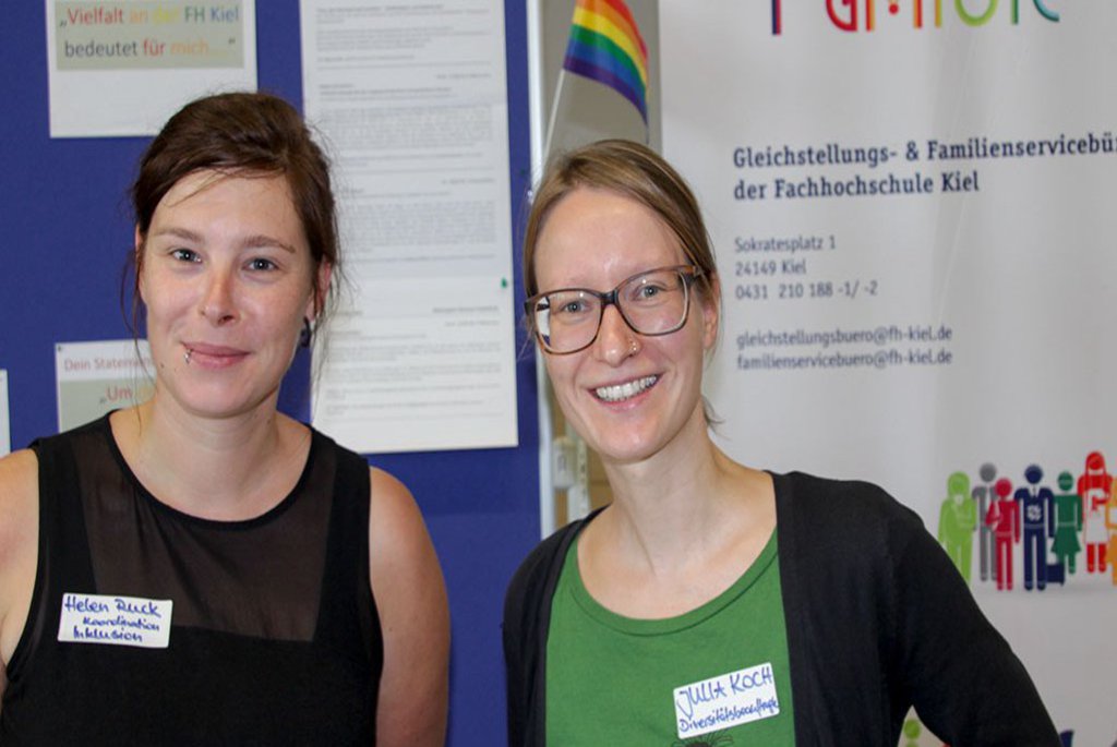 Zwei Frauen posieren vor einer Plakatwand.