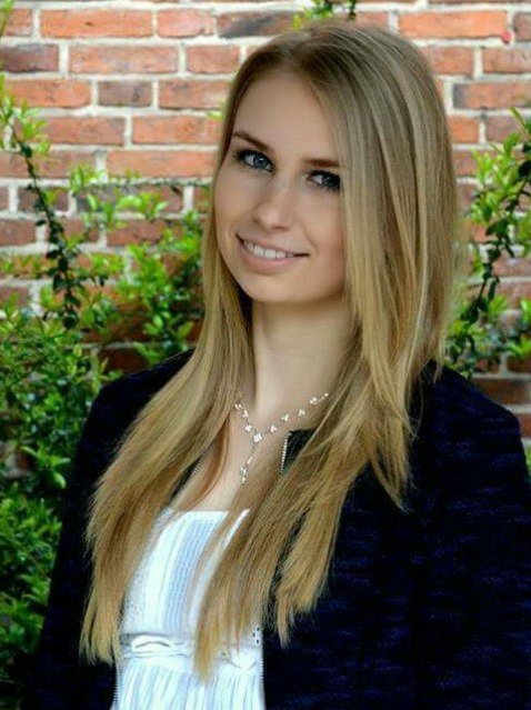 Eine Frau posiert vor einer Backsteinwand und lächelt ind die Kamera.