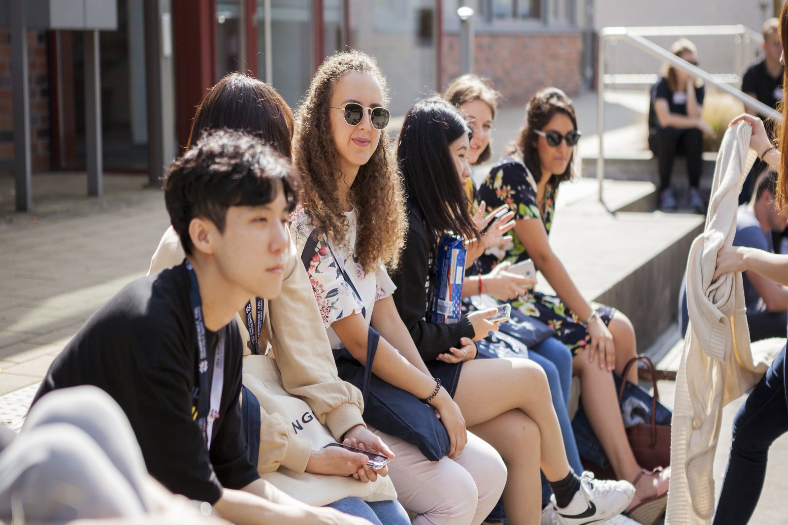 Campusimpression Internationale Studierende sitzen vor dem International Office in der Sonne.