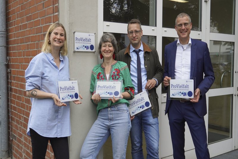 Auf dem Bild sind die Diversitätsbeauftragte, die Kanzlerin, der Vizepräsident und der Präsident vor dem Gebäude der Zentralverwaltung zu sehen.