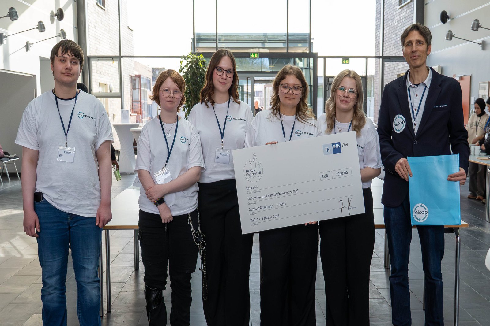 Die Schülerinnen und Schüler vom Team reloop stehen im Foyer des Audimax und halten ihren Symbolscheck in den Händen.