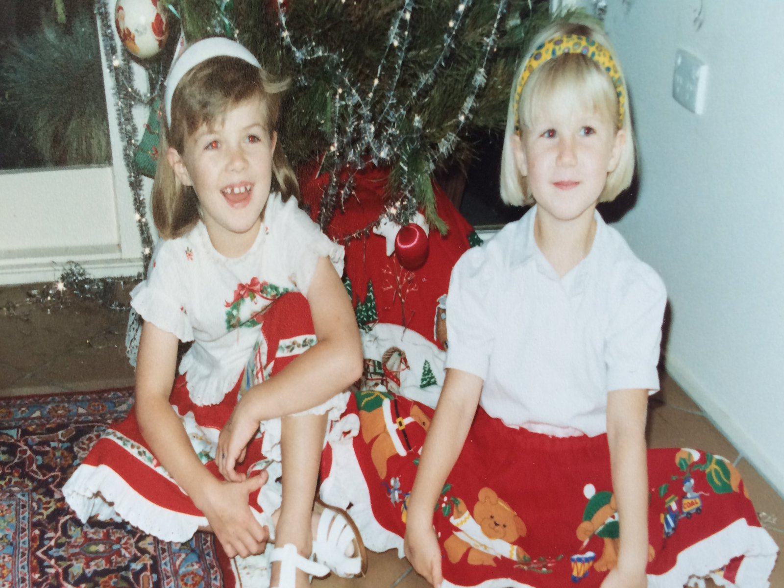 Zwei junge Mädchen posieren in ihren Weihnachtsoutfits vor einem geschmückten Tannenbaum.