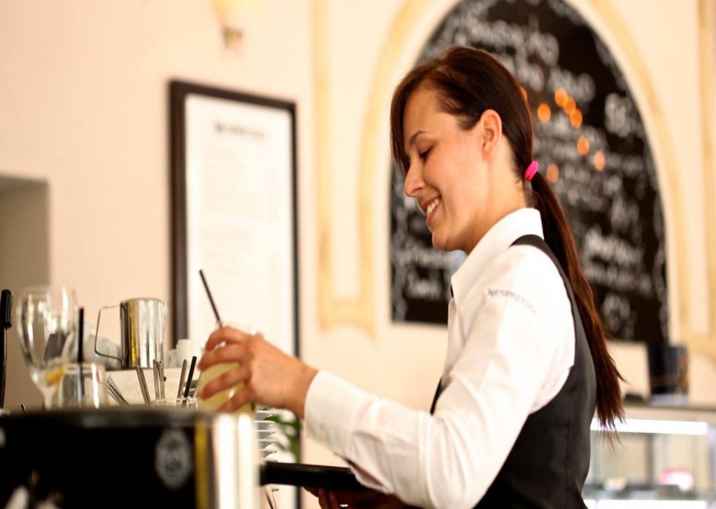Eine Frau steht in einer Gastronomie und räumt Geschirr von einem Servicewagen.