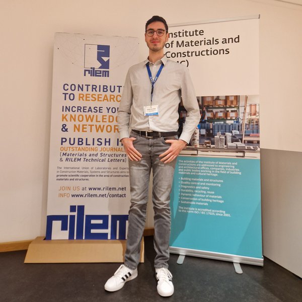 Bauwesen-Student Ahmet Can Akdal vor zwei Roll-ups auf der RILEM-Konferenz in der Schweiz 2025
