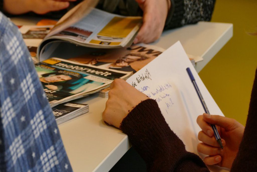 Zwei Hände halten ein Blattpapier an eine Tischkante.