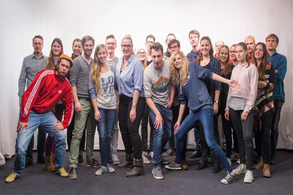 Eine Gruppe Studierender posiert angeregt vor einer weissen Wand.