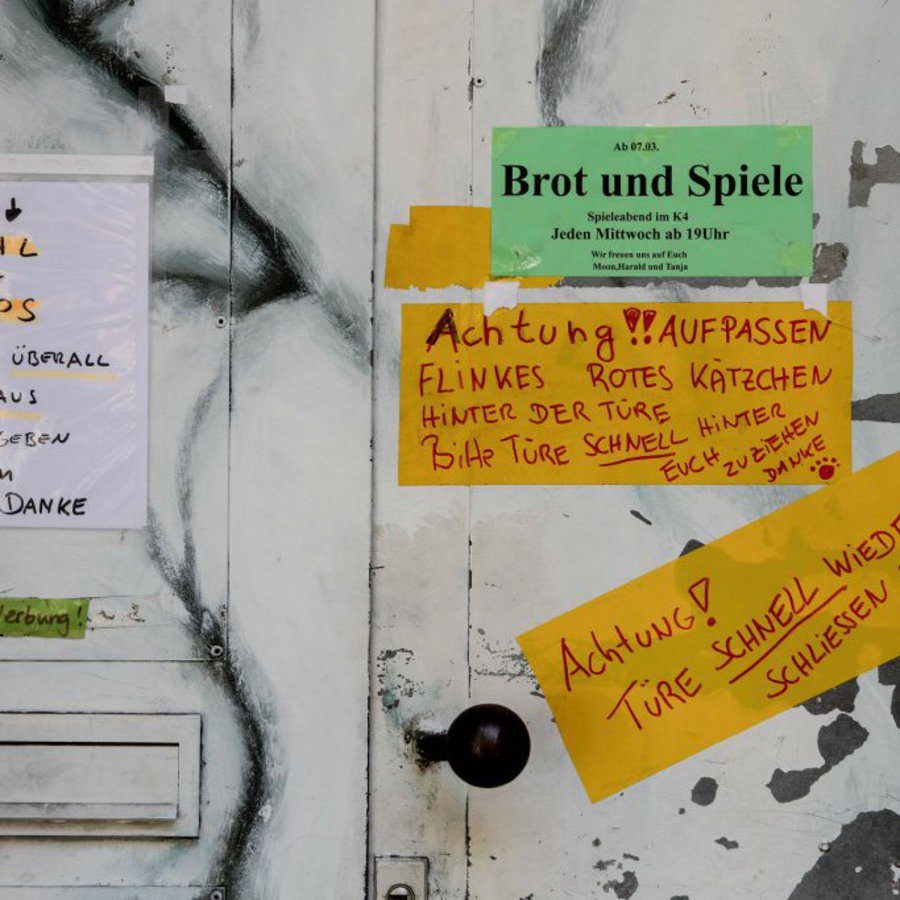 Eine weisse Tür, bei der der Lack langsam abbröckelt ist mit Informationspapieren beklebt.