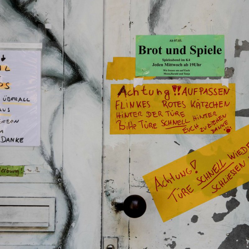 Eine weisse Tür, bei der der Lack langsam abbröckelt ist mit Informationspapieren beklebt.