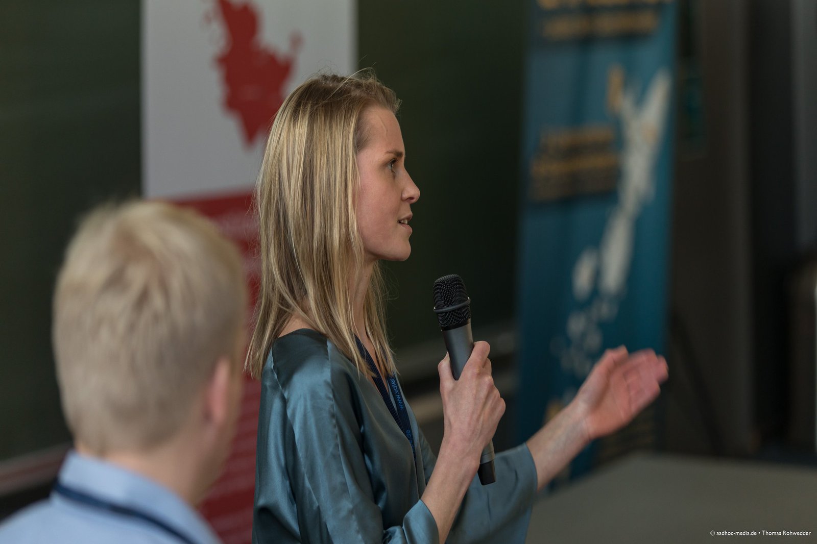 eine Frau hält eine Mikrofon und spricht zum Publikum.