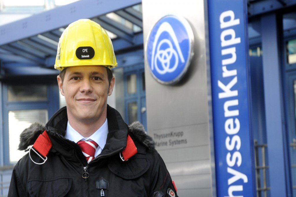 Ein Mann mit gelbem Helm und Sicherheitsjacke, schaut zufrieden in die Kamera.