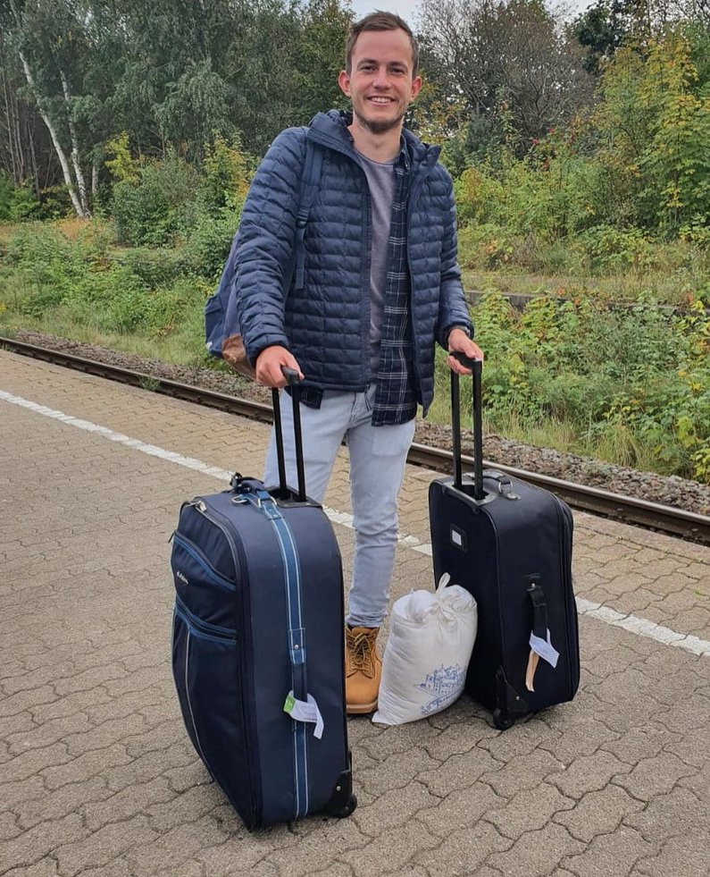 Frederik steht mit gepackten Koffern am Bahnsteig und grinst