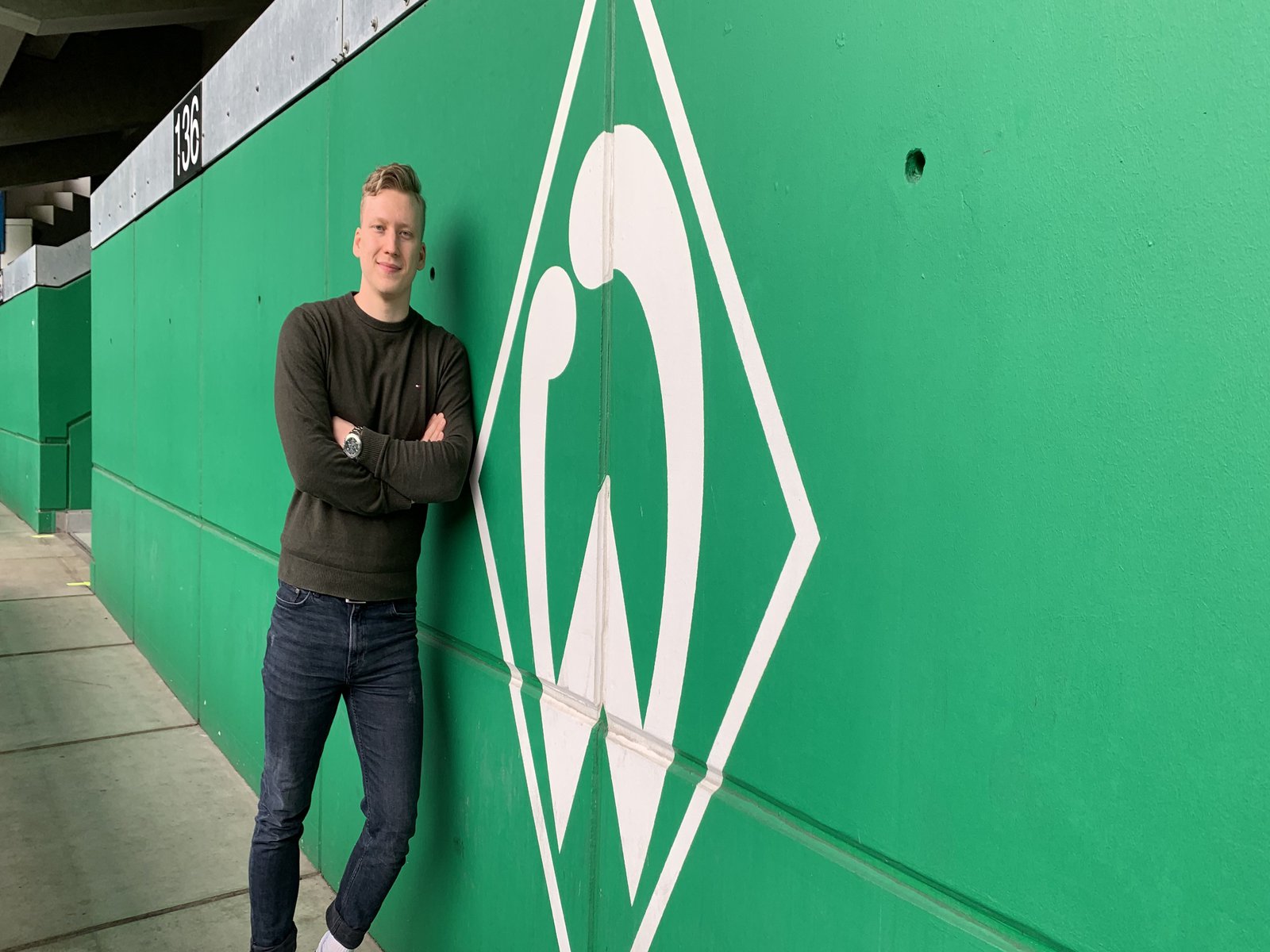 Lennard Worobic vor einer grünen Wand, auf der das Werder Bremen Logo zu sehen ist.
