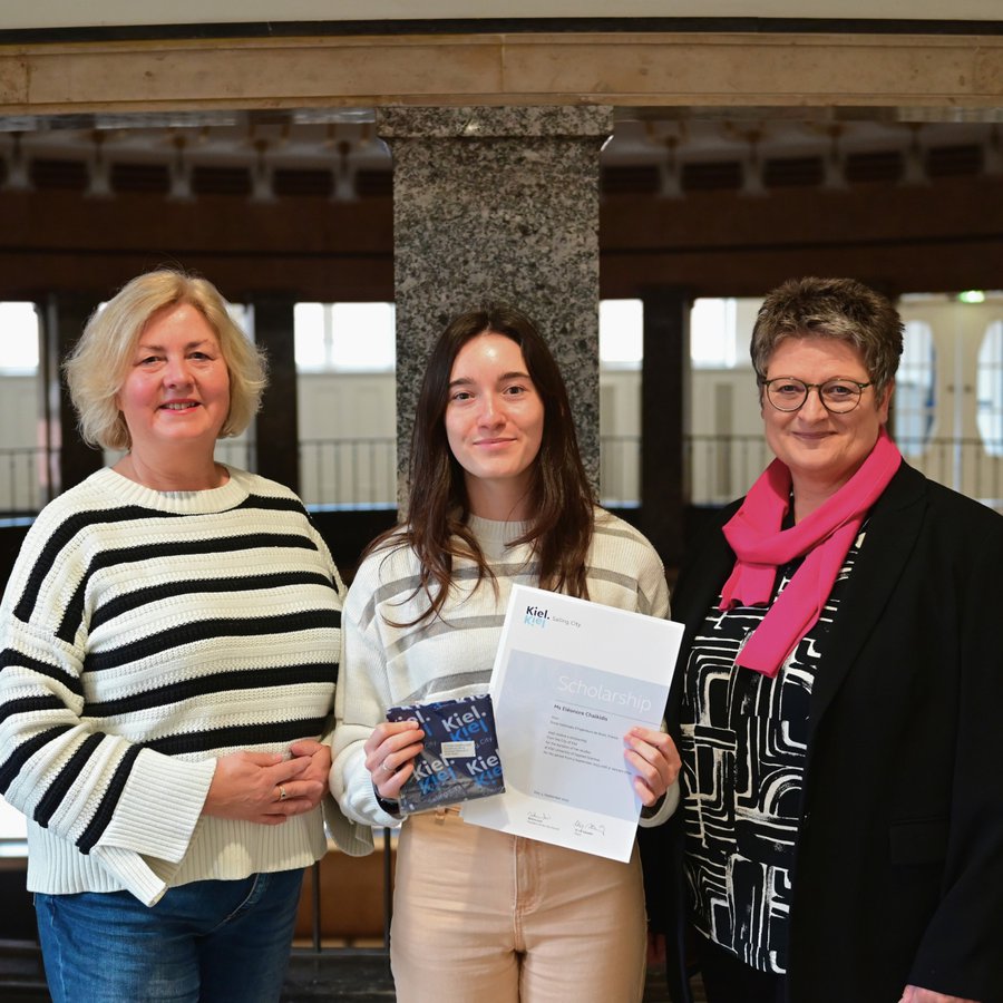 Das Foto zeigt drei Frauen im Foyer des Kieler Rathauses. (v.l.n.r. Stadtpräsidentin Bettina Aust, Stipendiatin Eléonore Chalkidis und Bürgermeisterin und Wissenschaftsdezernentin Renate Treutel).