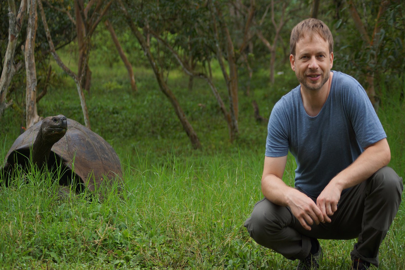 Ein Mann hockt im grünen in der Nähe von einer Riesenschildkröte.