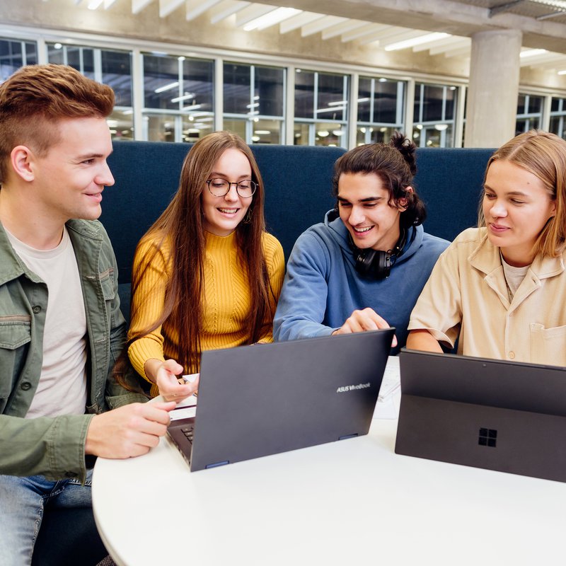 Vier junge Menschen sitzen an einem Tisch vopr zwei Laptops 
