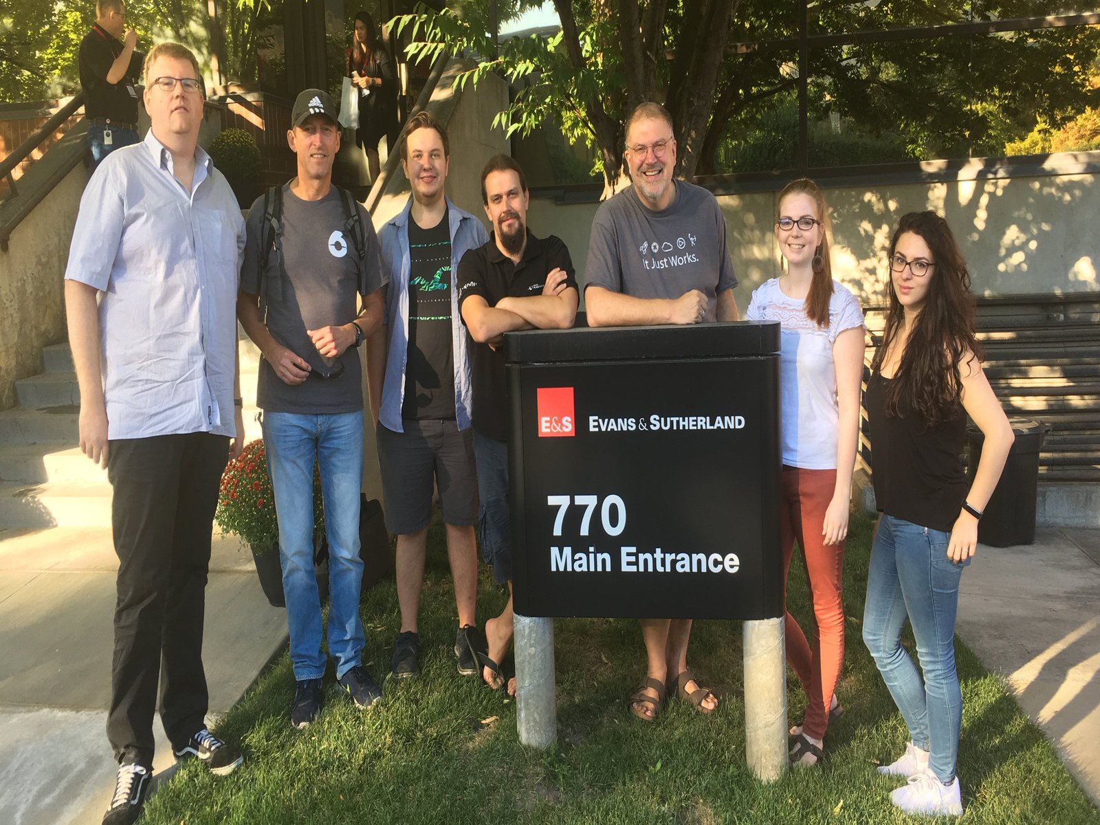 Personen in Sommerlicher Kleidung posieren vor einem Firmenschild.