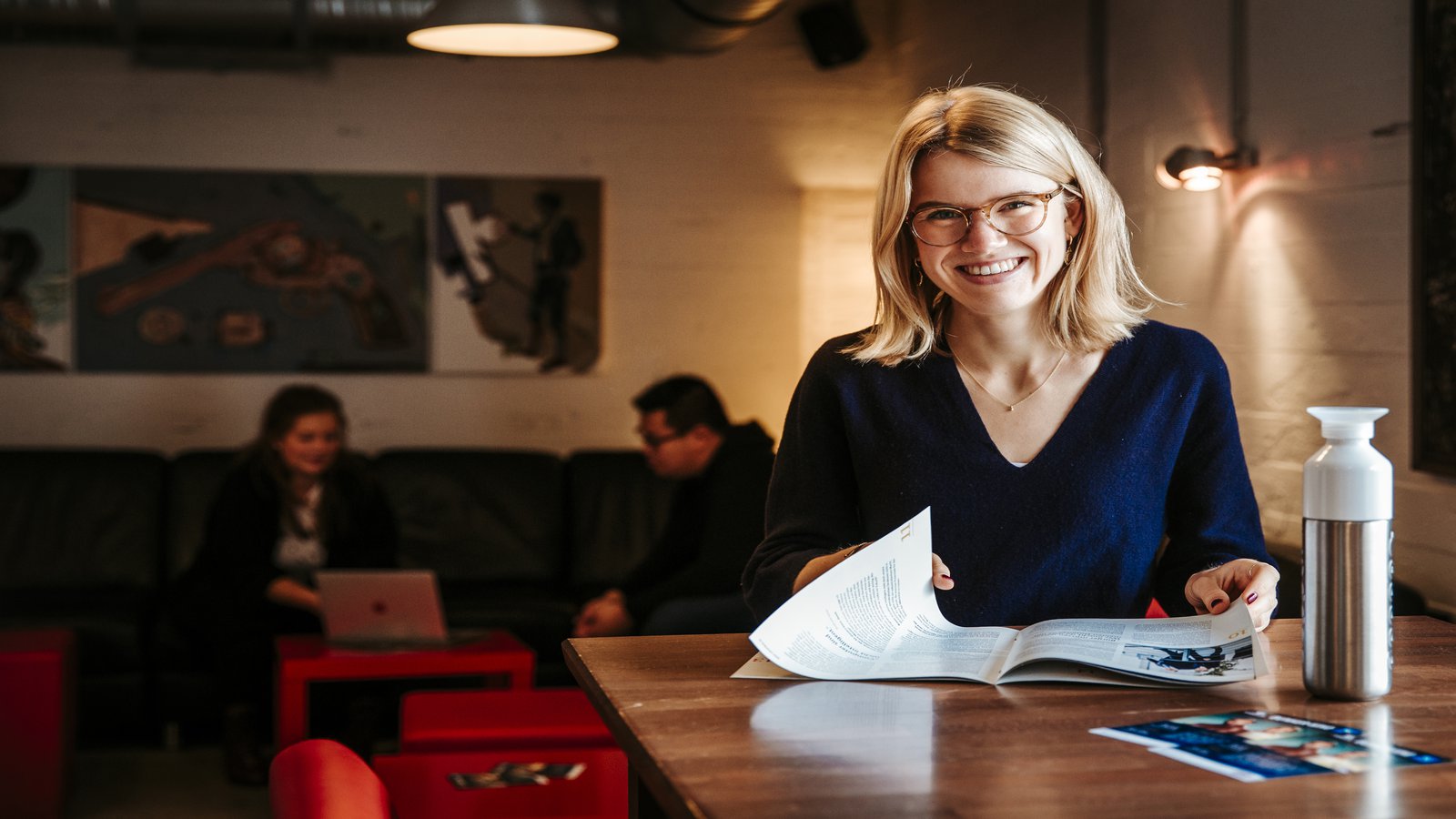 Foto: Hanna Börm eine Frau an einem Tisch blättert in einem Magazin und schaut von dort auf in die Kamera