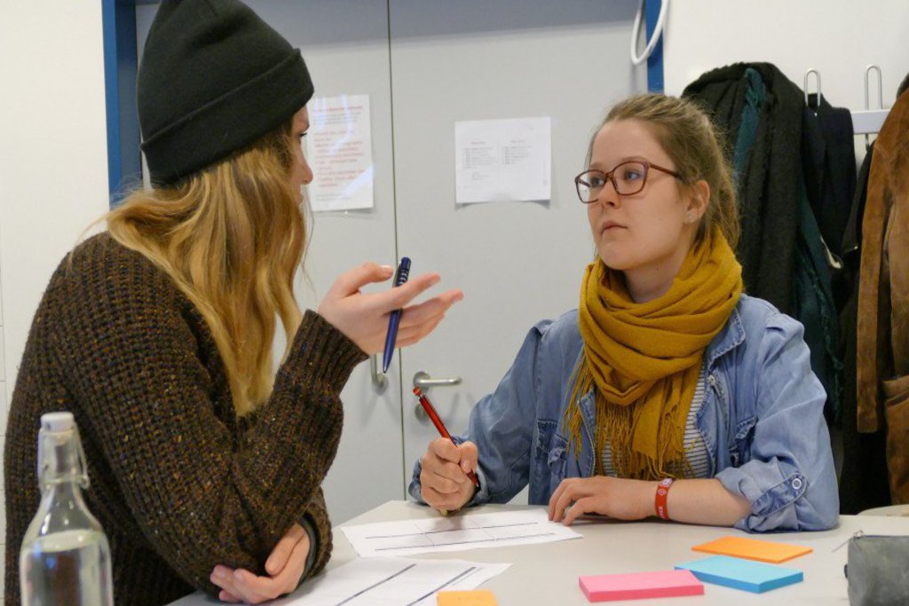 Zwei Studentinnen halten Kugelschreiber in der Hand und denken etwas aus.