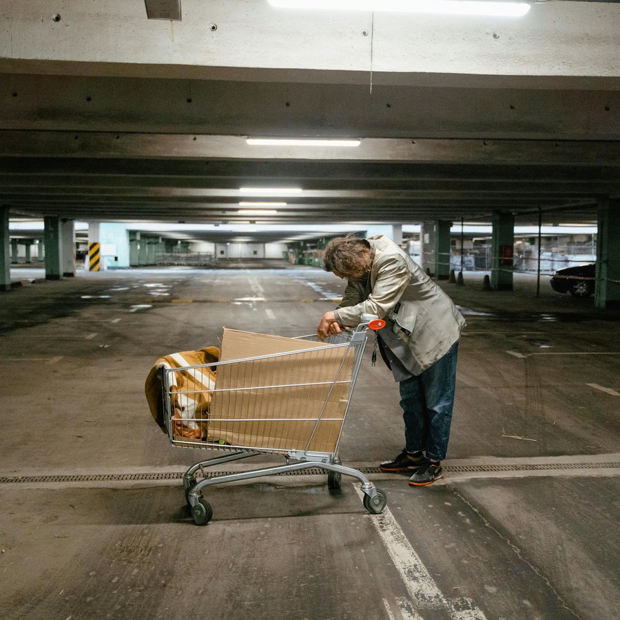 ein wohnungsloser Mann mit einen Einkaufswagen mit seinen Habseligkeiten in einer Tiefgarage