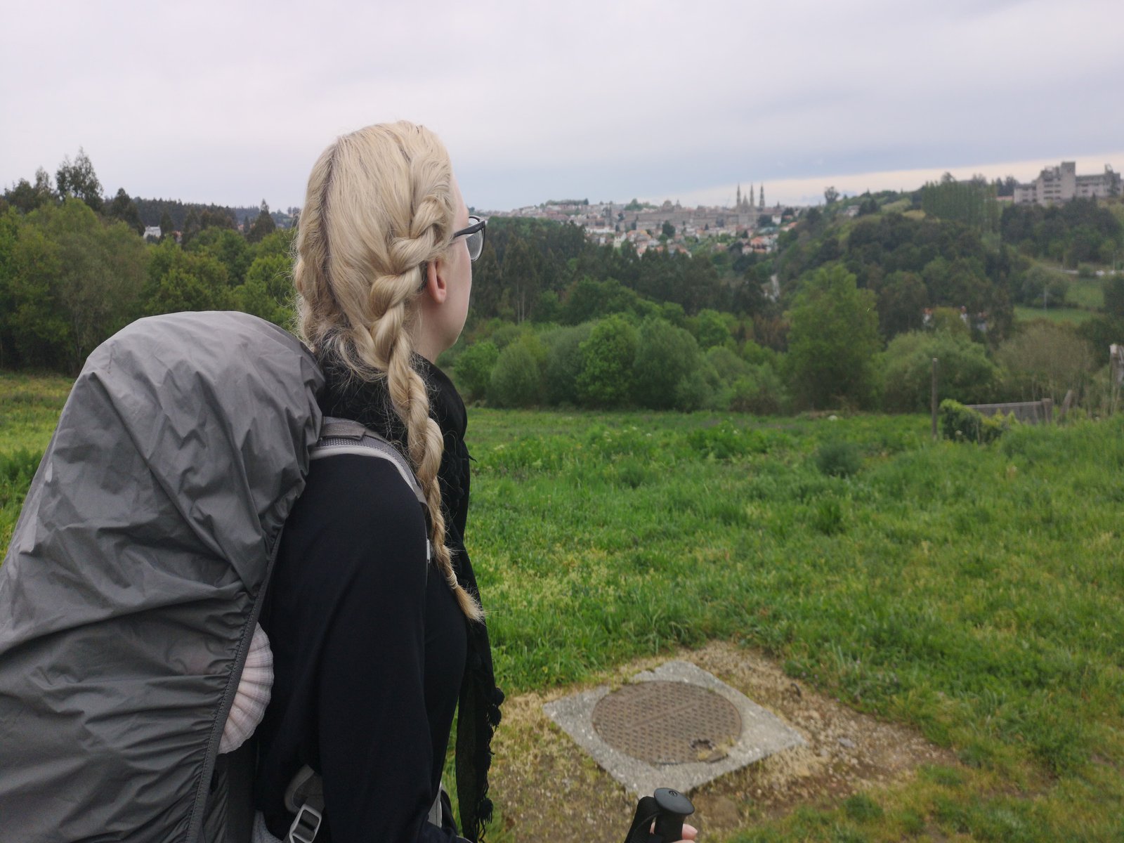 Eine Frau steht auf einer Rasenfläche und betrachtet aus der Ferne eine Kleinstadt.
