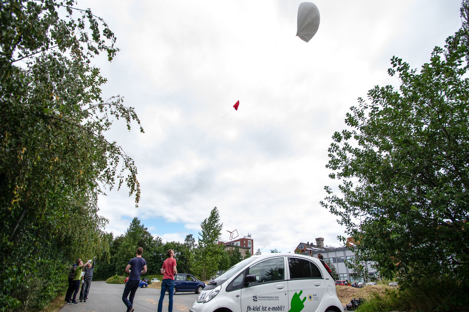 Im Vordergrund steht ein Kleinwagen der Initiative "fh-kiel ist e-mobil", im Hintergrund lassen Studierende den Wetterbalon steigen.