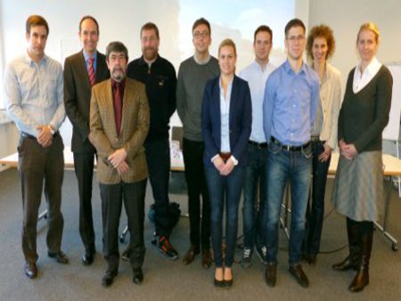 Die Projektgruppe versammelt sich vor der Leinwand, in einem Konferenzraum.