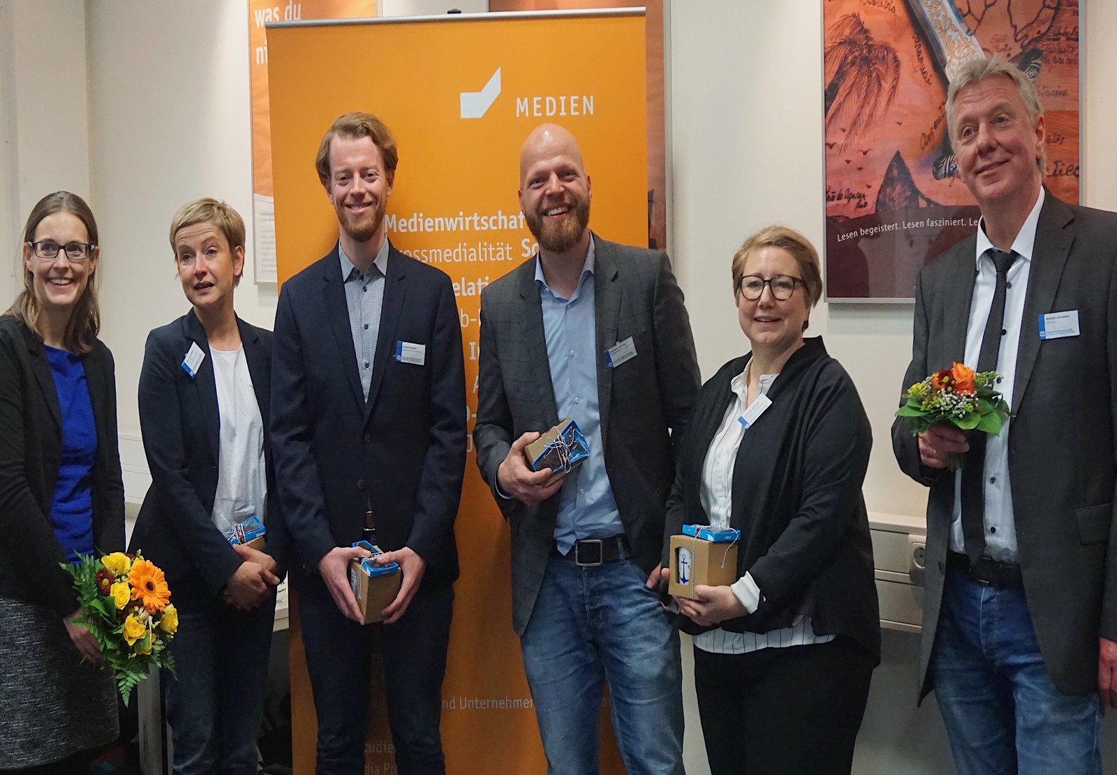 Eine Gruppe von Lehrenden posiert vor einem Medien Banner.