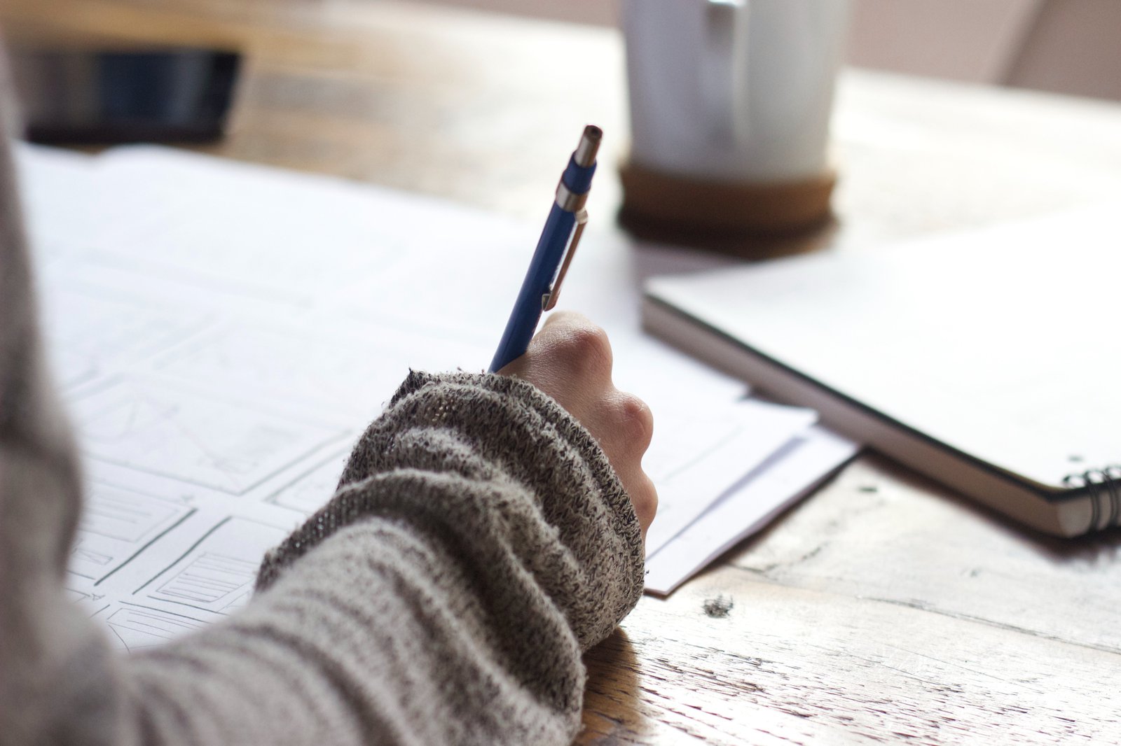 Eine Hand schreibt Notizen, auf einem Holztisch auf.