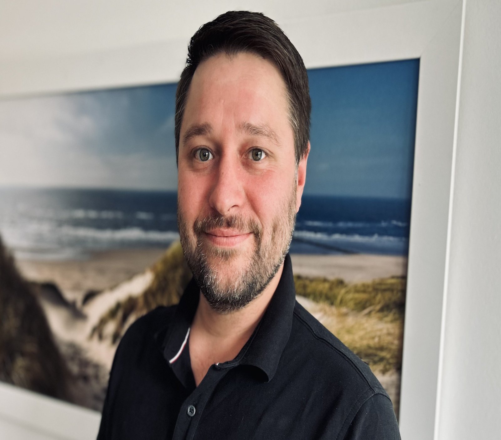 ein Mann mit Bart vor einem Bild, das eine Küste zeigt