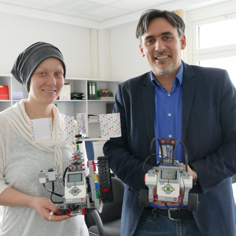 Eine Mann und eine Frau präsentieren in ihrem Büre jeweils einen Roboter.
