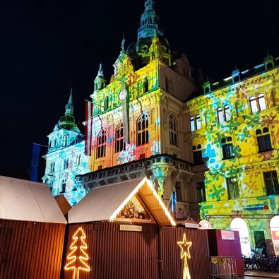 Bunte Dekorationen und angestrahlte Fassaden im Dunkeln beim Grazer Weihnachtsmarkt