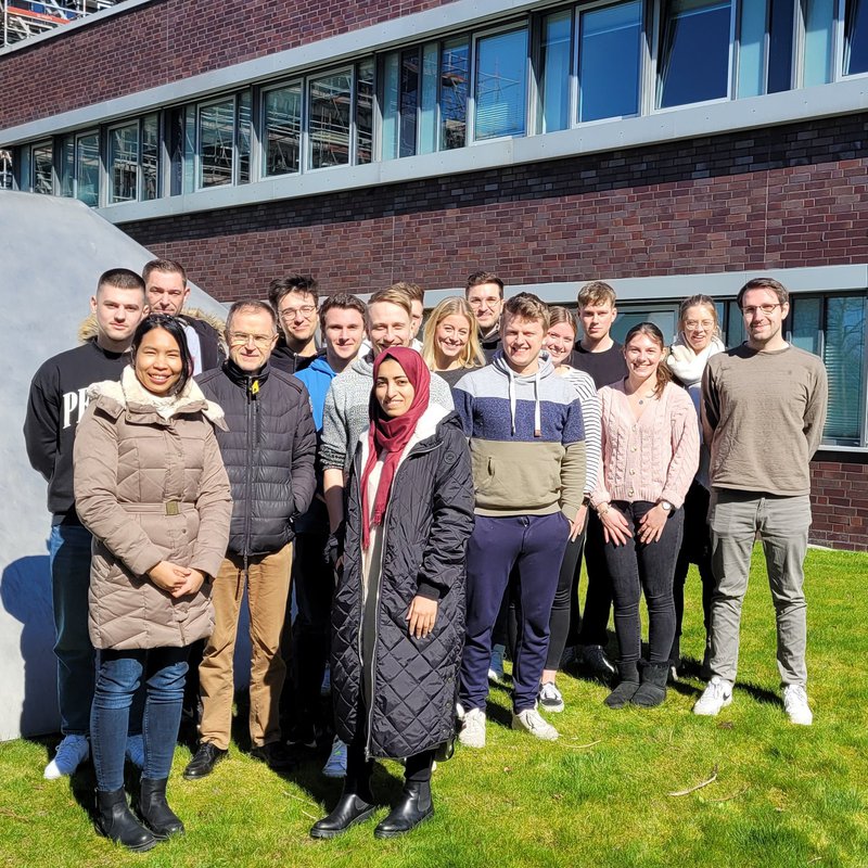 eine Gruppe Studierender steht auf dem Rasen vor Gebäude 18 der Fachhochschule Kiel