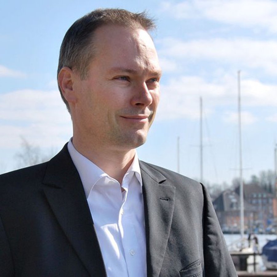 Ein Mann in Jackett und Hemd posiert an der Schwentinemündung und schaut in die Ferne.